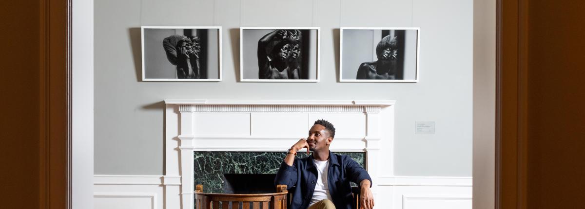 Photograph of person sitting in gallery with three photographs on the wall